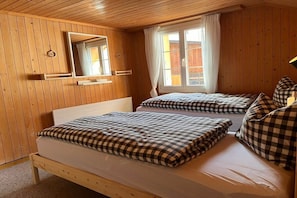 Ein Zimmer mit Holzwandverkleidung, zwei Betten mit karierten Bettbezügen, einem Spiegel und einem Vorhangfenster.