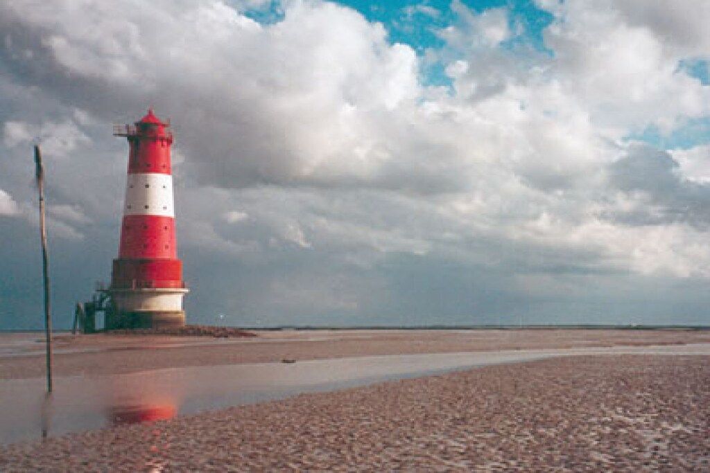 Un faro en una playa pedregosa bajo un cielo nublado.