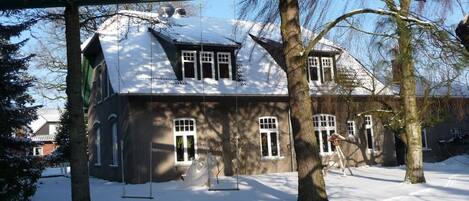 Ein schneebedecktes Haus mit einer großen Veranda und einer Schaukel.