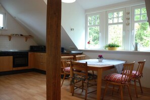 Een keuken met houten kastjes, een eettafel met stoelen en een raam met uitzicht op groen.