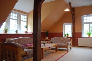 A cozy room with a sloped ceiling, wooden beams, and large windows with potted plants. - Holiday apartment in Jade with barbecue (Jade)