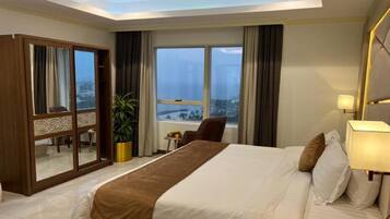 Habitación de hotel con una cama grande, un escritorio, una silla, una planta y vistas a la ciudad desde la ventana.