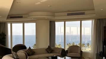 Een ruime woonkamer met een groot raam dat uitzicht biedt op de oceaan en palmbomen, een comfortabele zithoek en een salontafel.