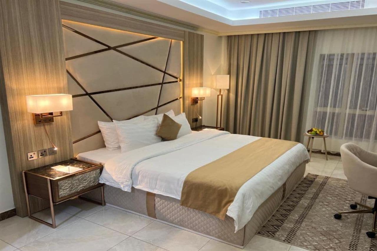 A modern hotel room with a large bed, bedside lamps, a small table, and a chair.