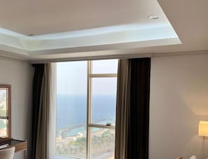 A hotel room with a large window, a desk, and a lamp.