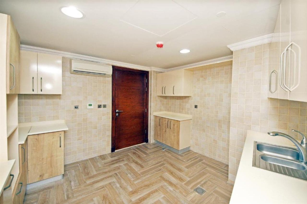 Een keuken met een visgraatvloer, houten kastjes, een wit aanrecht en een roestvrijstalen spoelbak.