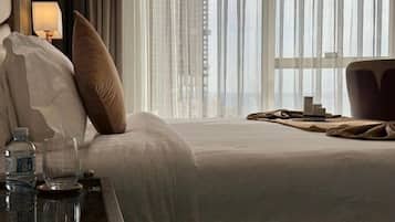 Een hotelkamer met een bed, een nachtkastje met een lamp en uitzicht door dunne gordijnen.