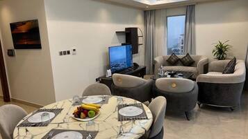 Una sala de estar moderna con comedor, televisor de pantalla plana y un gran ventanal con cortinas.