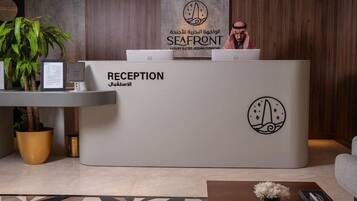 Un mostrador de recepción con un cartel que indica 'RECEPTION' y 'SEAFRONT' en varios idiomas, una computadora portátil, una planta y un documento enmarcado.