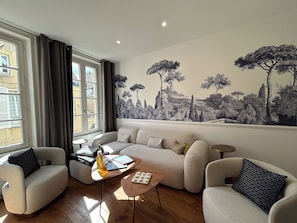 A living room with a sofa, armchairs, a coffee table, and a wall mural. - Villa Ursuline: Charm and Comfort in the Heart of the City (Bayeux)