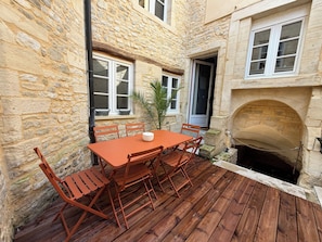 Ein Steingebäude mit einer Holzterrasse, einem Tisch mit Stühlen und einem Kamin.