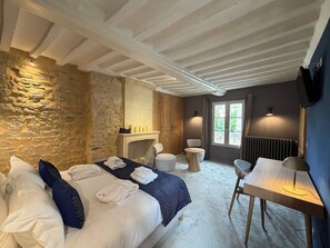 Ein Hotelzimmer mit Steinwand, Kamin, Bett mit Handtüchern, Schreibtisch und Stuhl.