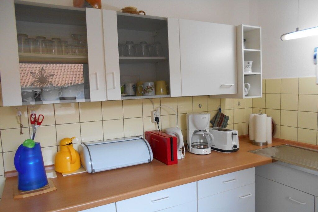 Une cuisine avec des meubles blancs, un plan de travail sur lequel se trouvent un grille-pain, une machine à café et un appareil électroménager rouge.