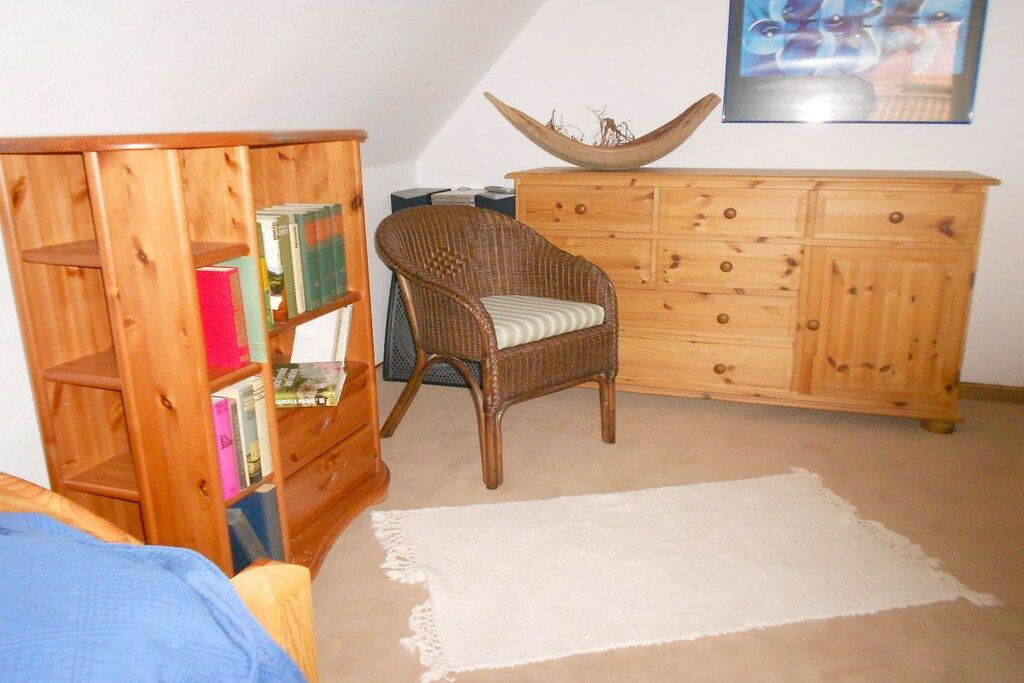 Een kamer met een houten boekenkast, een rieten stoel, een houten kast en een witte vloerkleed.