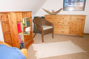 Una stanza con una libreria in legno, una sedia in vimini, un armadietto in legno e un tappeto bianco.