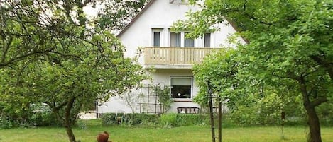 A two-story house with a balcony, surrounded by trees and a lawn.
