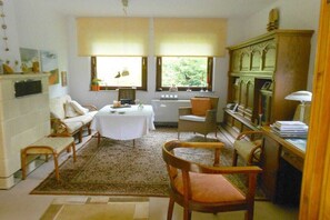 Ein Zimmer mit einem weißen Sofa, einem runden Tisch, einer Holzkabine und einem Fenster mit Blick auf Grünflächen.
