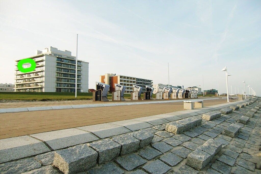 Un chemin pavé avec des blocs de pierre, un bâtiment moderne avec une enseigne verte et une rangée de pierres tombales.
