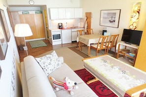 A compact living space with a kitchenette, a dining area, a sofa with a dog toy, and a television. - Kaiserhof with sea view - Spa Zone 1 (Norderney)