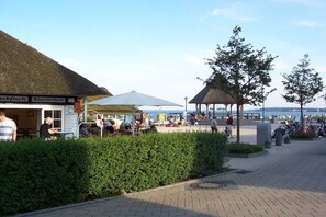 Ein Restaurant am Wasser mit Terrassensitzmöglichkeiten, einem Gebäude mit einem Reetdach und einem Kiosk.