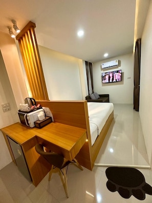 A hotel room with a wooden desk, a bed, a TV, and an air conditioning unit.