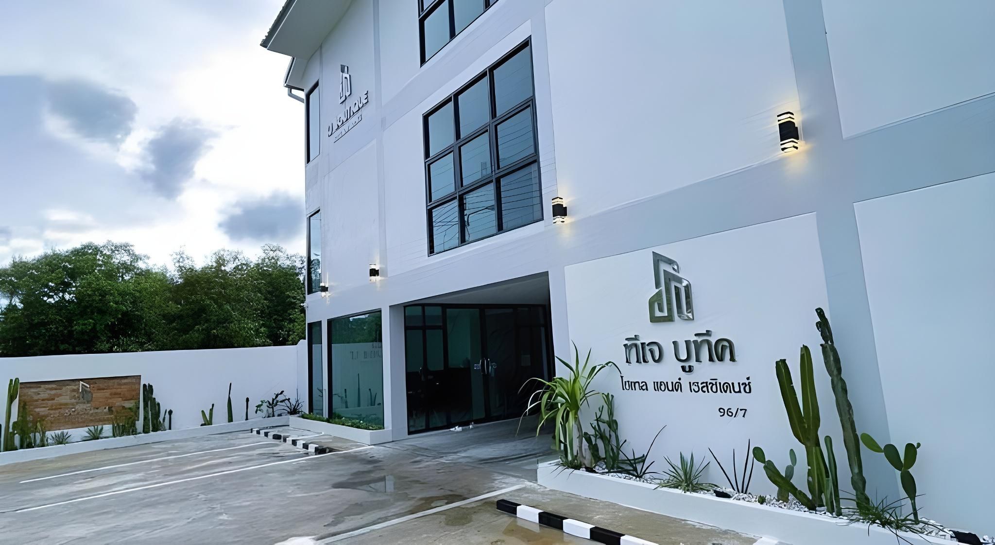 Ein modernes Gebäude mit weißer Fassade, großen Fenstern und einem Schild mit thailändischen Schriftzeichen.