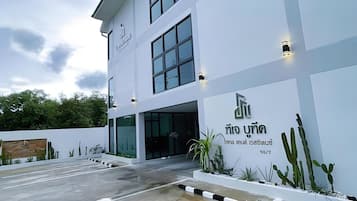 Ein modernes Gebäude mit weißer Fassade, großen Fenstern und einem Schild mit thailändischen Schriftzeichen.