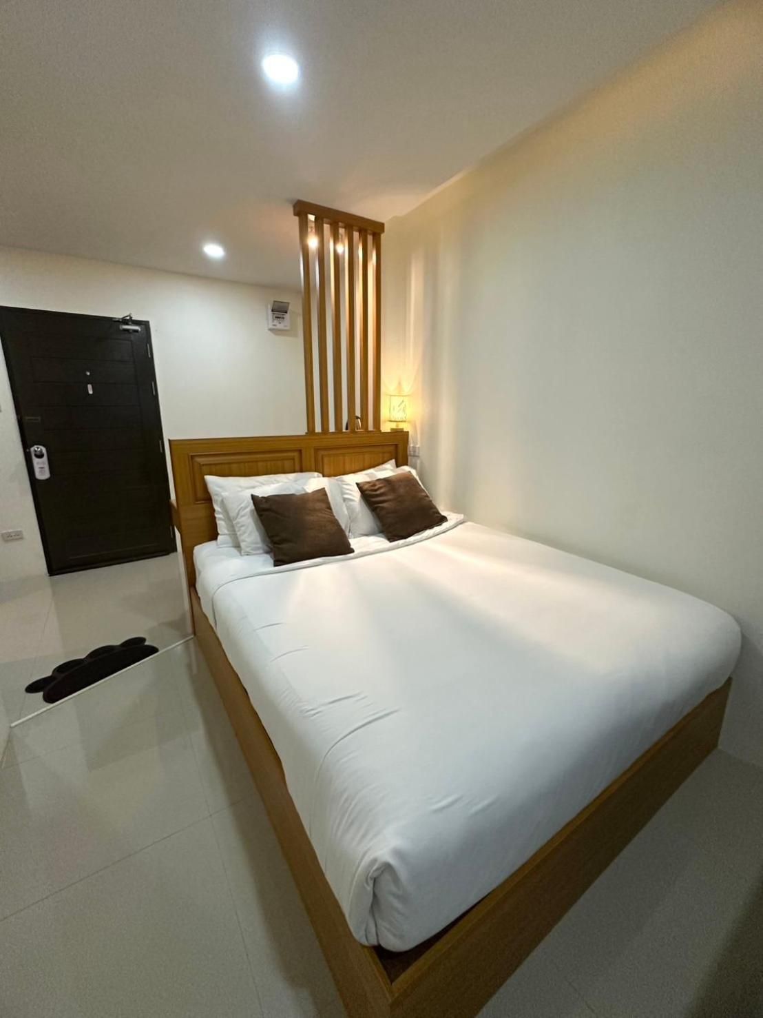 A hotel room with a wooden bed, white bedding, a black door, and a nightstand with a lamp.
