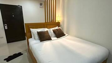 A hotel room with a wooden bed, white bedding, a black door, and a nightstand with a lamp.