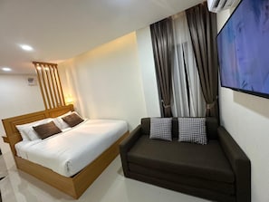A modern hotel room with a wooden bed, a sofa, a TV, and a window with curtains.