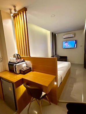 A hotel room with a wooden desk, a chair, a bed, a television, and an air conditioning unit.