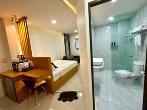 A hotel room with a bed, desk, chair, and a shower area.