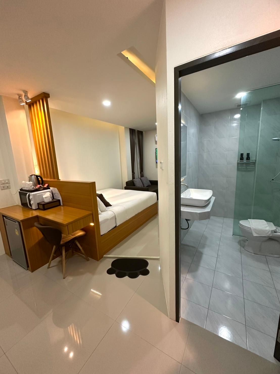 Ein Hotelzimmer mit Bett, Schreibtisch, Stuhl, einer kleinen Küchenzeile und einem Badezimmer mit Toilette und Dusche.