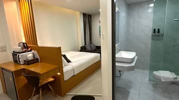 Ein Hotelzimmer mit Bett, Schreibtisch, Stuhl, einer kleinen Küchenzeile und einem Badezimmer mit Toilette und Dusche.