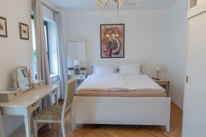 Een slaapkamer met een bed, nachtkastjes, een bureau, een stoel en een schilderij aan de muur.