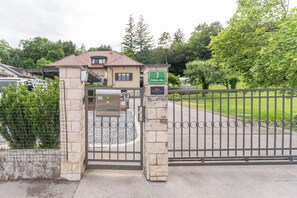 Een toegangspoort naar een perceel, met een stenen muur, een metalen hek en een groen bord met het adres.