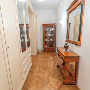 A hallway with a wooden floor, a wooden cabinet with glass doors, a wooden console table with a vase, and a mirror on the wall. - Parkside Haven-your Ljubljana Home Away from Home – 4 Bedrooms & Free Parking (Ljubljana)