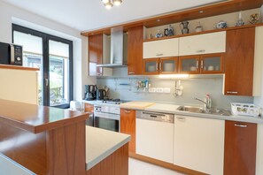A modern kitchen with wooden cabinets, a stove, a dishwasher, and a window with blinds.