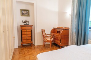 A bedroom with a wooden dresser, a chair, a bed, a painting on the wall, and a window with curtains. - Parkside Haven-your Ljubljana Home Away from Home – 4 Bedrooms & Free Parking (Ljubljana)