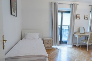 Un dormitorio con cama, cómoda, escritorio con silla y puerta que da a un balcón.