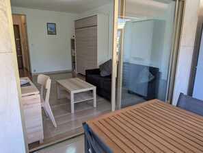 A modern living room with a wooden table, a sofa, and a glass door leading to a balcony. - Charming 1-bedroom apartment with AC in peaceful Menton Garavan. (Menton)