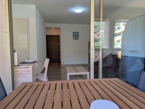 Ein modernes Interieur mit einem Holztisch, einem weißen Stuhl, einer Glastür, die auf einen Balkon führt, und einer Tür mit Glasfenster.
