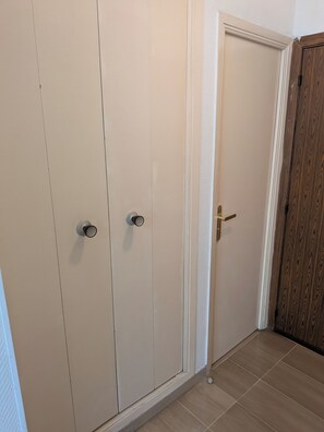 Ein Flur mit einem beigefarbenen Kleiderschrank, einer Holztür und einem gefliesten Boden.