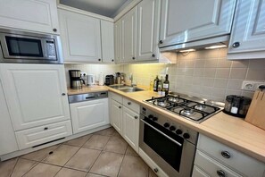 A kitchen with white cabinets, a microwave, a coffee maker, a gas stove, and a dishwasher. - Hansen Friesen House (Westerland)