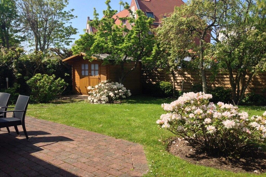 Un jardin avec un chemin en briques, une structure en bois et des arbustes en fleurs.