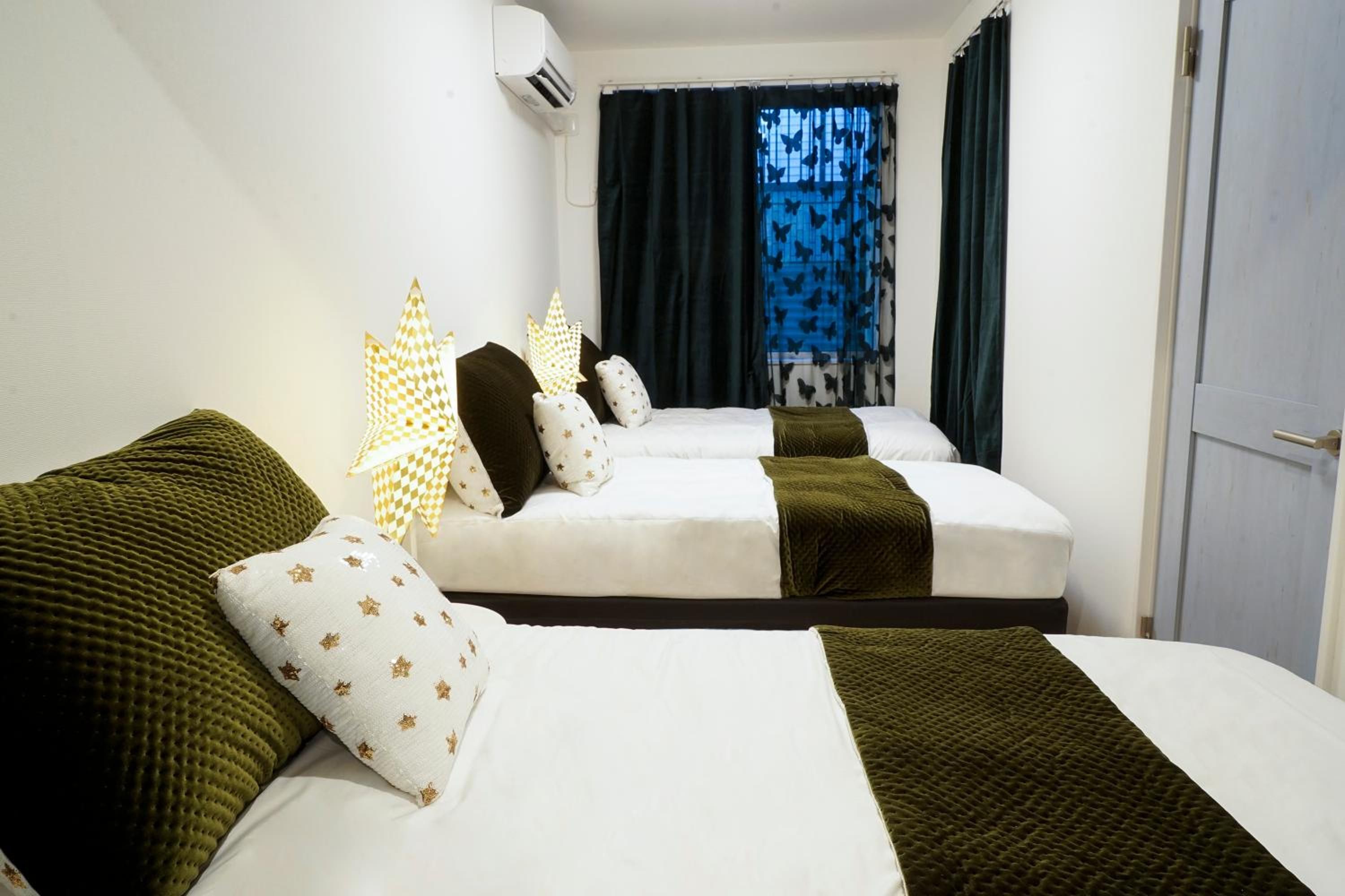A hotel room with two beds, a window with curtains, and an air conditioning unit.