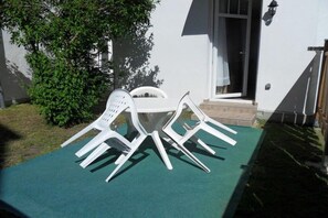 A patio with a white table and chairs, a small step leading to a door, and a wall-mounted light fixture. - Apartment "Baltic Sea Dune" (Kühlungsborn)