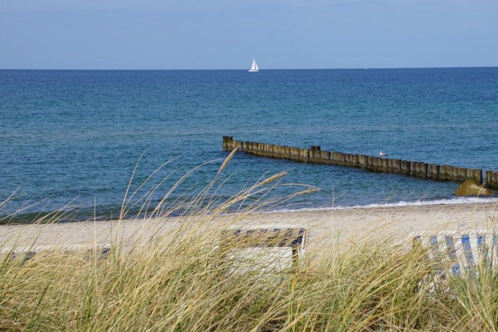 A coastal scene with a sandy beach, a wooden jetty, and a sailboat in the distance.
