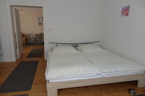 A single bed with a metal frame and a patterned bedspread, a wooden floor, and a door leading to a dining area. - Apartment "Baltic Sea Dune" (Kühlungsborn)