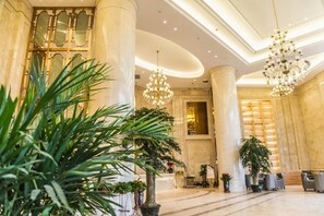 A spacious lobby with high ceilings, large columns, and elegant chandeliers.